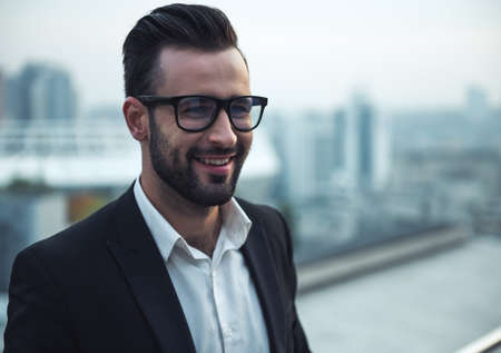 Handsome businessman in suit and glasses is smiling while standing on the balconyの写真素材