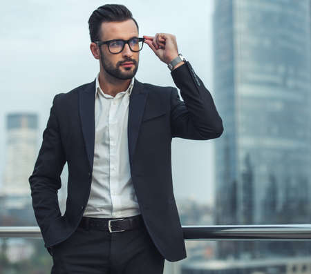 Handsome businessman in suit and glasses is looking away while standing outdoorsの写真素材