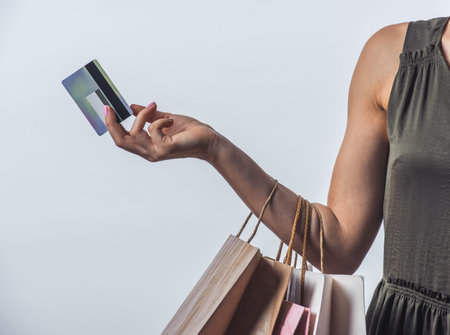 Cropped image of young woman in dress holding a credit card and shopping bags, on light backgroundの写真素材