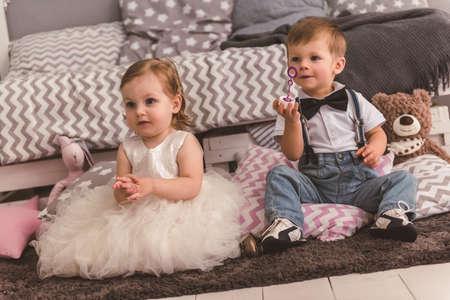 Cute kids in elegant clothes are playing with soap bubbles in the children's roomの写真素材