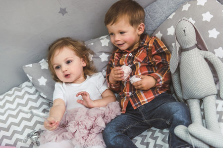 Cute kids are playing together in the children's room. Boy is holding sweets and smilingの写真素材