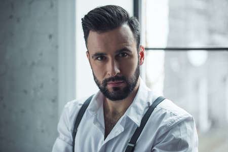 Portrait of handsome confident man looking at camera, window in the backgroundの写真素材