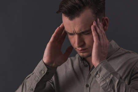Tired young businessman in smart shirt is massaging his temples, on gray backgroundの写真素材