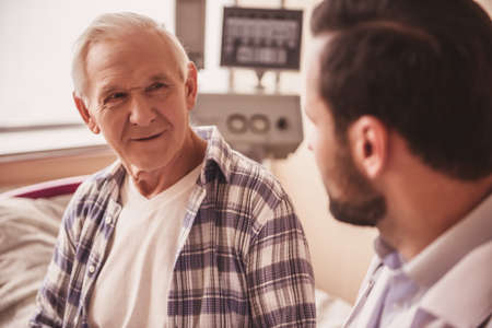 Handsome old man is talking with a doctor while sitting in hospital wardの写真素材