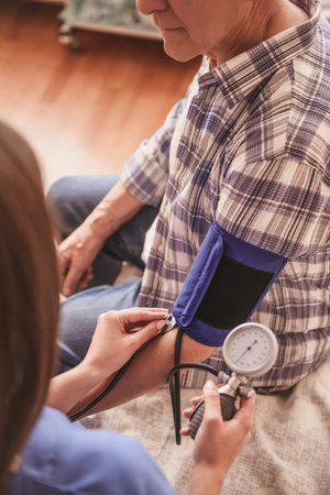 Cropped image of an old man sitting in hospital ward while a doctor is measuring his blood pressure