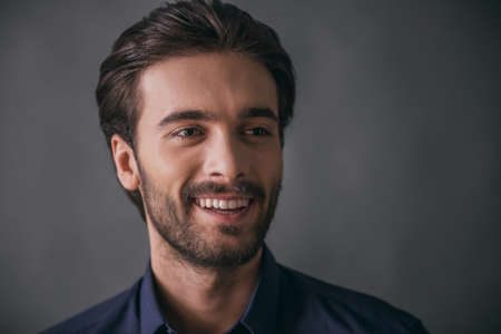 Handsome confident businessman with bristle, in dark blue shirt is looking away and smiling, on gray backgroundの写真素材