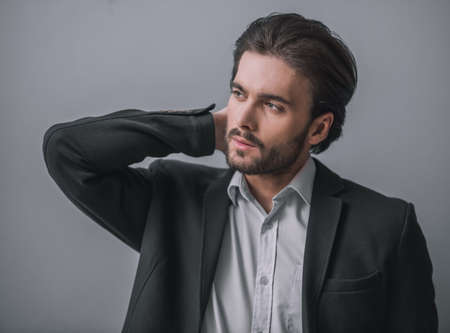 Handsome bearded businessman in suit is looking away, on gray backgroundの写真素材
