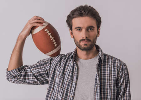 Handsome bearded man in casual clothes is holding a football ball and looking at camera, on light backgroundの写真素材