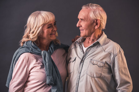 Beautiful old man and woman in casual clothes are looking at each other and smiling, on gray backgroundの写真素材