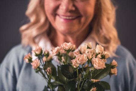 Cropped image of beautiful old lady in casual clothes holding flowers and smiling, on gray backgroundの写真素材