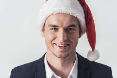 Handsome guy in suit and Santa hat is looking at camera and smiling, isolated on whiteの写真素材