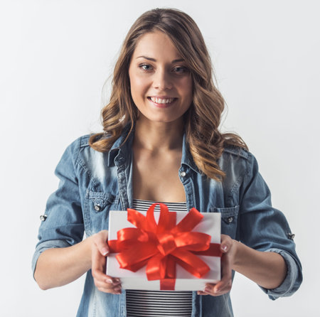 Beautiful young woman in casual clothes is holding a gift box and smiling, isolated on white