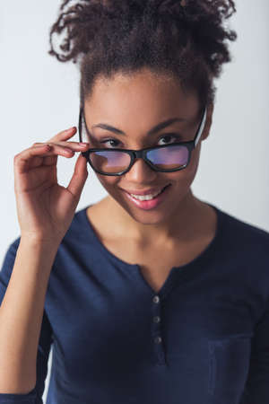 Beautiful Afro-American girl in casual clothes and eyeglasses is looking at camera and smiling, isolated on whiteの写真素材