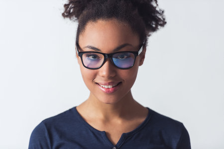 Beautiful Afro-American girl in eyeglasses is looking at camera and smiling, isolated on white