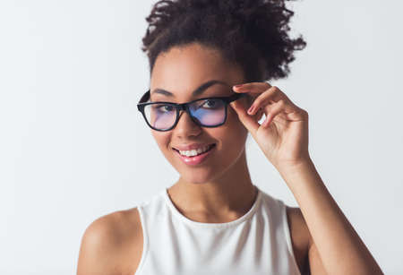 Beautiful Afro-American girl in eyeglasses is looking at camera and smiling, isolated on whiteの写真素材
