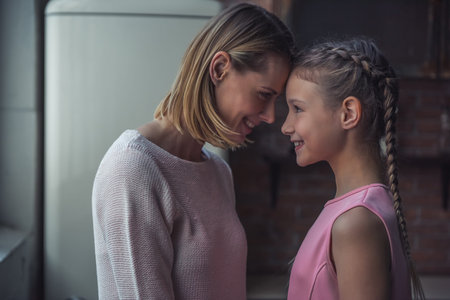 Mom and daughter are  touching with their foreheads, looking at each other and smiling while...