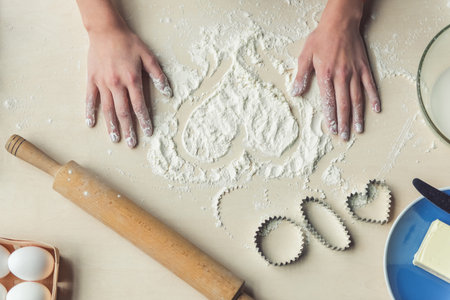 Cropped image, top view of little girl making heart of flour while baking