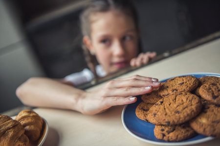 Little girl is reaching for the cookies from under the table, hand in focusの写真素材