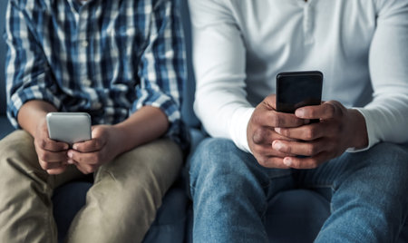 Cropped image of Afro American father and son in casual clothes using smartphones while sitting on...