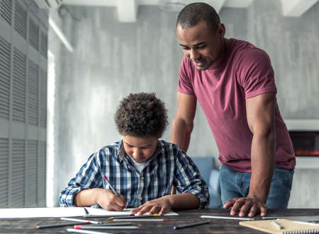 Handsome Afro American man is smiling while watching his son drawing, at homeの写真素材