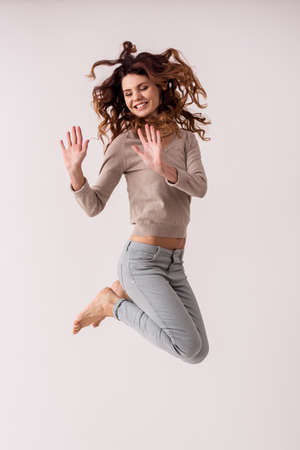 Young emotional pretty girl while jumping on white background smile at cameraの写真素材