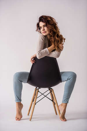 Portrait of a young beautiful girl sitting on a chair and smiling at the camera on a white backgroundの写真素材