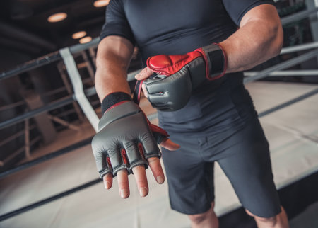Cropped image of boxer putting on boxing gloves while preparing to train in gym