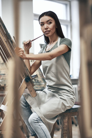 Young beautiful woman painting artist while working in a studio, smiling to the camera