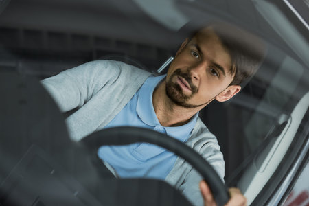 Young man is sitting in the car in the showroom.