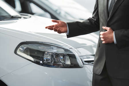 Young man consultant in showroom is standing near car.の写真素材