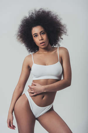 Afro American woman in white lingerie is posing at camera, on a grey backgroundの写真素材