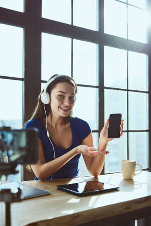 Young beautiful girl blogger working in office while shooting at camera listens to music in headphonesの写真素材