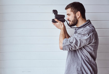 Young emotional man while shooting with old camera on light backgroundの写真素材