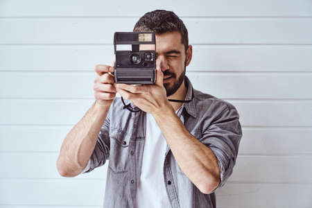 Young emotional man while shooting with old camera on light backgroundの写真素材