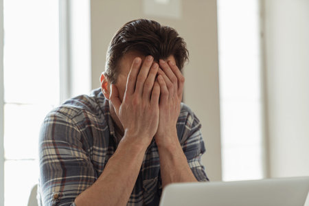 Young male businessman while working remotely with laptop sitting at table at home in the kitchen...