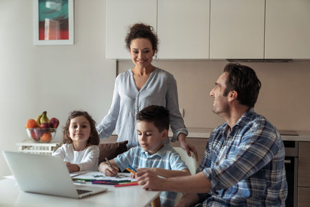 Mom helps little daughter and son draw while father works at home with computer and documents...