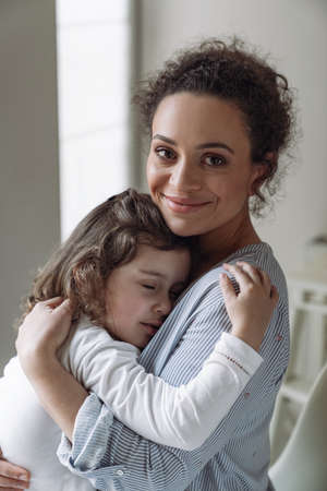 Good family, mother and daughter. Little daughter hugging her mother with a smile and closed eyes at homeの写真素材