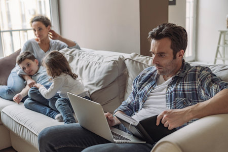 Young successful freelancer man working at home sitting on sofa against the backdrop of his wife and...