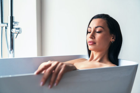 Young beautiful woman relaxes taking a bath in the bathroom at home on the background of a large...