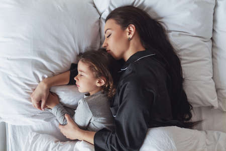 Happy morning. Young beautiful mother and her little daughter sleep in bed at home, mother hugs her daughter.の写真素材