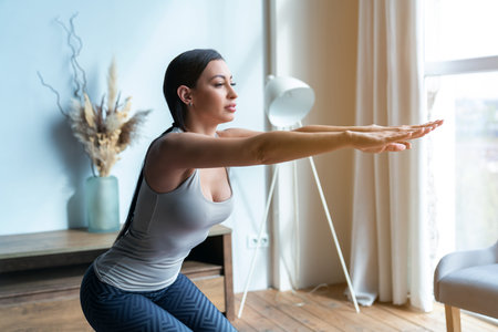 Young beautiful fitness woman squats during yoga in the living room at home.