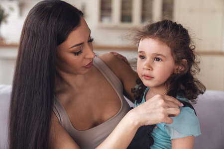 Happy young mother and her little daughter spend time together and have fun sitting hugging on the couch in the living room at home.の写真素材