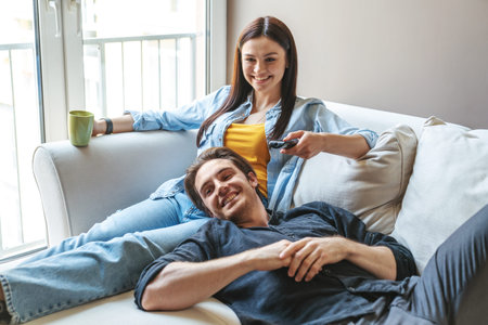 Young happy couple guy and girl hugging lying together on the couch at home in the apartment holding...