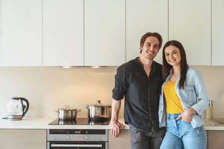 Portrait of young cheerful couple guy and girl standing at home in the kitchen in the apartment and hugging something discussing.の写真素材
