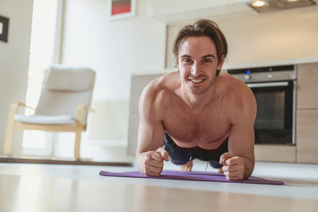 Young man during sports at home in the apartment on the background of the kitchen.
