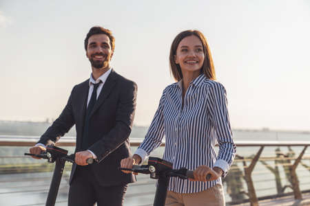 Young business man and business woman while riding electric scooters on the background of the morning cityの写真素材