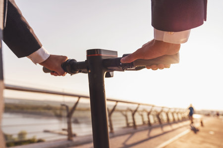 Cropped image of a man in a business suit and shoes stepping on an electric scooter standing on a...