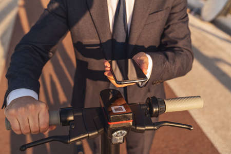 Cropped image of a man in a business suit and shoes stepping on an electric scooter standing on a city streetの写真素材