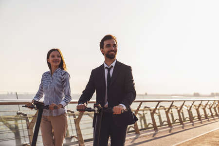 Young business man and business woman while riding electric scooters on the background of the morning cityの写真素材