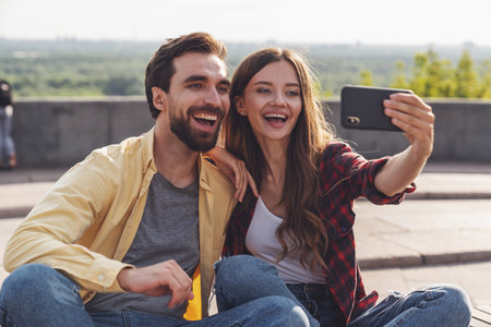 Young couple having fun talking on a bench and taking a selfie using the phone while walking in the...